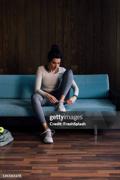 young woman sitting on blue couch and tying shoelace - shoelace stock pictures, royalty-free photos & images