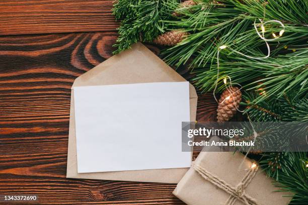 paper blank card and envelope. christmas greeting card. natural pine tree green branches, winter decorations of pine cones and fairy lights over dark brown wood background. - christmas picture frame stock pictures, royalty-free photos & images