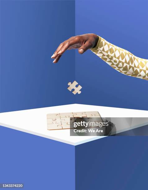 hand dropping piece into jigsaw puzzle - puzzle business stockfoto's en -beelden