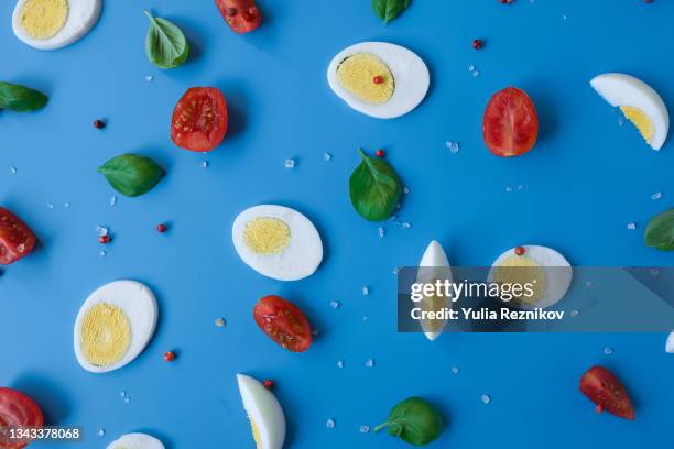 flat lay of the boiled eggs, tomato, basil, salt and red pepper on the blue background - egg white background stock-fotos und bilder