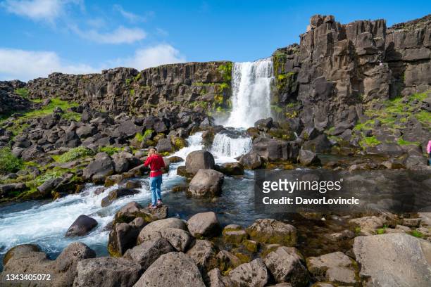 mature woman standing on rock and enjoying oxararfoss waterfall at mid-atlantic ridge, iceland - thingvellir national park stock pictures, royalty-free photos & images