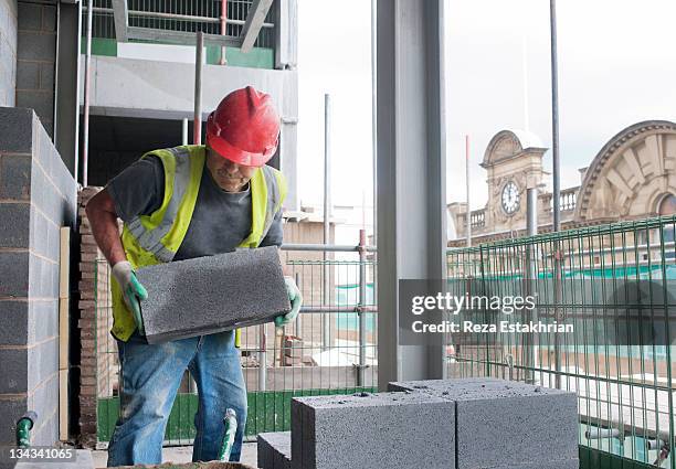 construction worker moves cinder block on site - construction material foto e immagini stock
