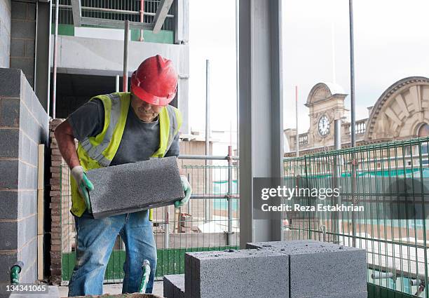 construction worker moves cinder block on site - construction material stockfoto's en -beelden