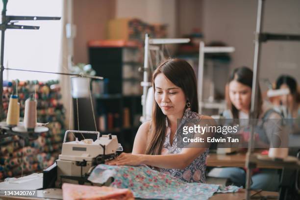 asian chinese female blue collar worker working in sewing studio in a row - textielfabriek stockfoto's en -beelden