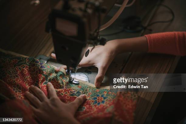 vue rapprochée haut angle main d’une adolescente chinoise asiatique tenant des coutures de batik couture sur machine à coudre éclairée par une lumière led - batik photos et images de collection
