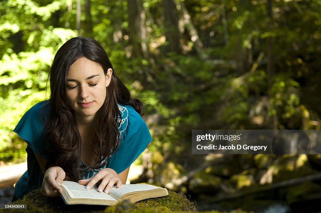 Young woman reading bible by stream