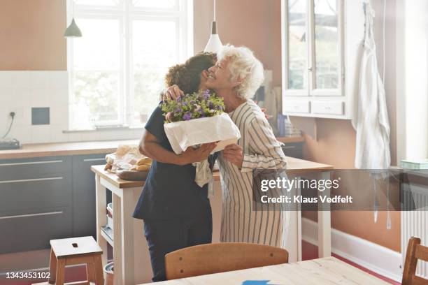 senior woman embracing female nurse with bouquet - receiving fotografías e imágenes de stock