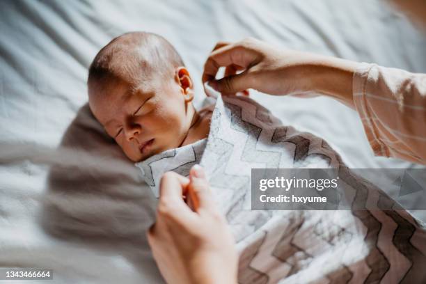 mutter wickelt ihr neugeborenes baby aufs bett - bedeckt, verhüllt oder überdacht stock-fotos und bilder