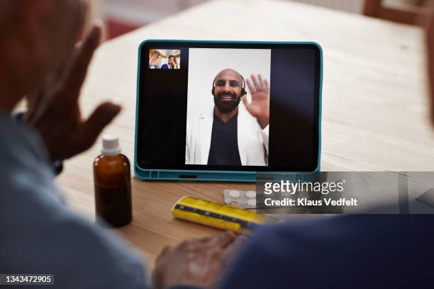Doctor waving at senior man on video call