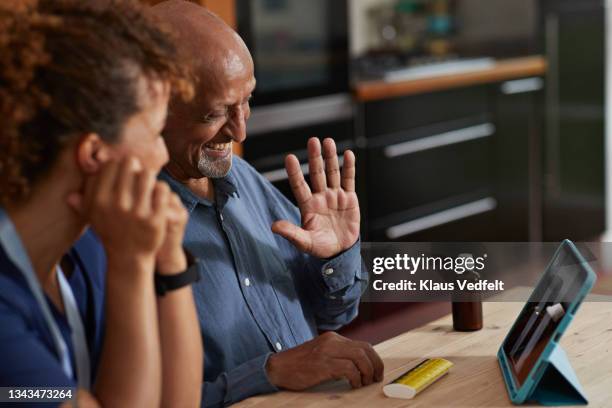 senior man waving at doctor on video call - conference dining table stockfoto's en -beelden