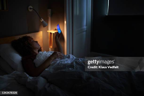 woman waking up through alarm ring on smart phone - mature woman screen stock-fotos und bilder