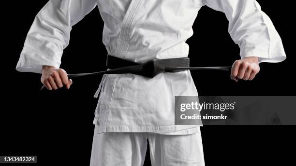 male karate player standing against black background - black belt stock pictures, royalty-free photos & images