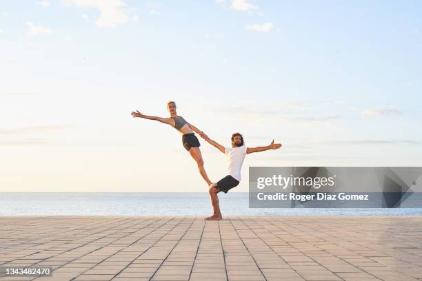young couple exercising yoga on the beach at sunset - acrobate photos et images de collection
