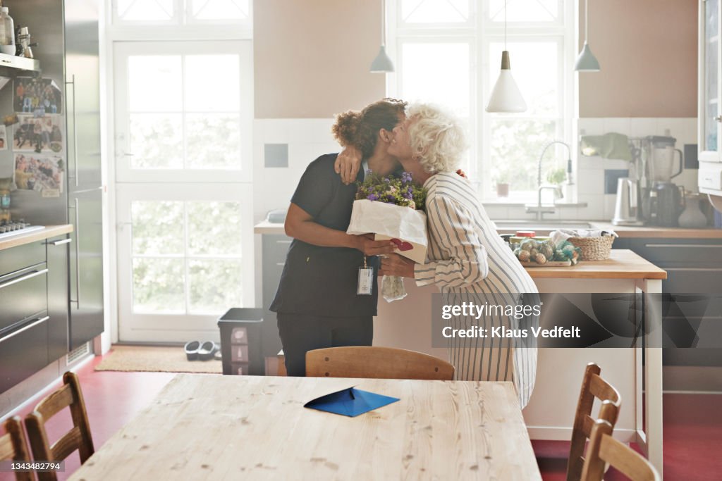 Senior woman greeting caregiver with bouquet