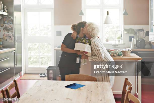 Senior Woman Greeting Caregiver With Bouquet, Stock-Foto