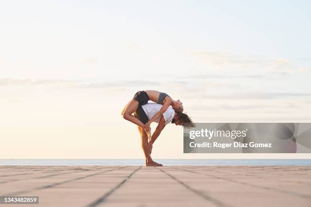 man crouching while his partner climbs on his back against sky - acroyoga stock pictures, royalty-free photos & images