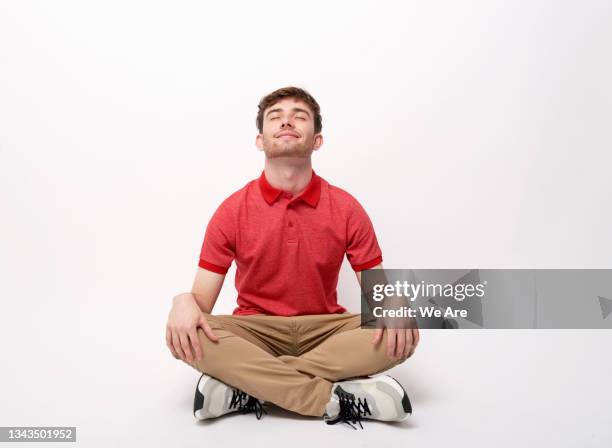 young man in causal clothing sitting cross-legged meditating - cross legged stock pictures, royalty-free photos & images