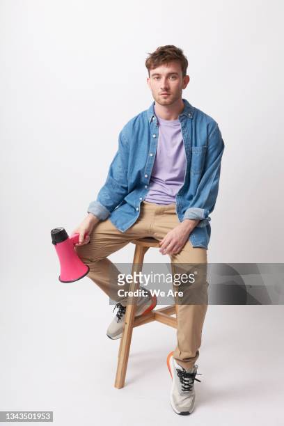 young man sits on stool despondently holding a megaphone by his side - assento imagens e fotografias de stock