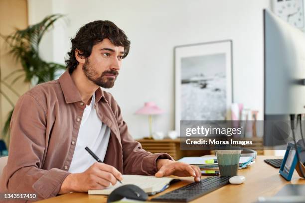 male entrepreneur writing in book at home office - freelancer stockfoto's en -beelden