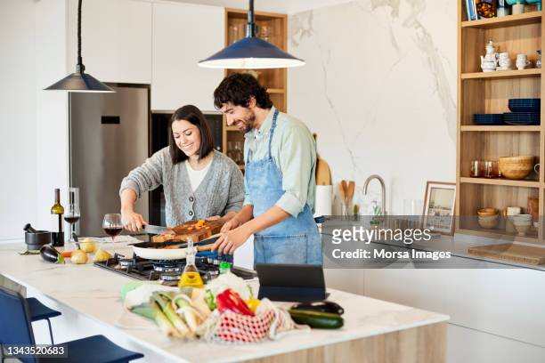 woman helping boyfriend in preparing meal at home - couple in kitchen foto e immagini stock