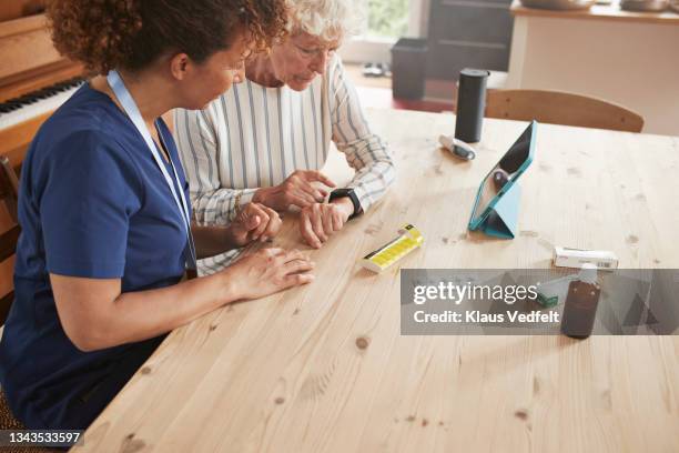 woman learning to use smart watch from caregiver - wearable computer stock-fotos und bilder