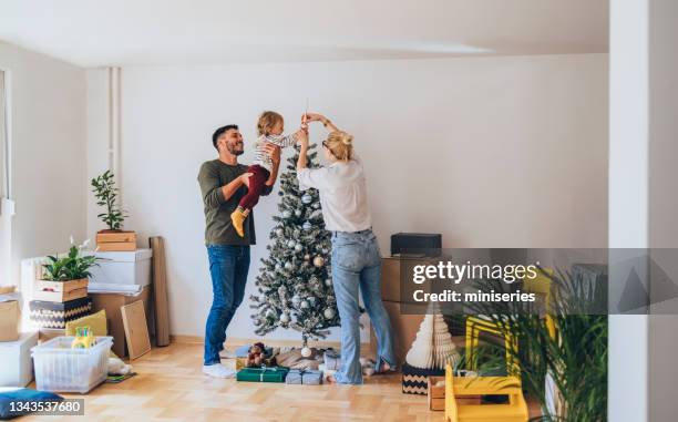 famiglia felice che decora l'albero di natale nella nuova casa - decorare l'albero di natale foto e immagini stock