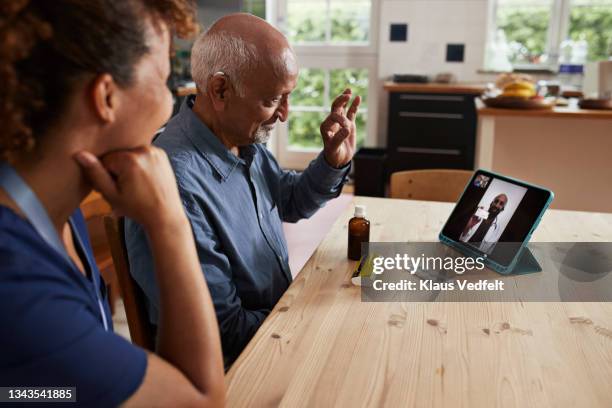 man gesturing while male doctor on video call - nurse with old male patient home care stock-fotos und bilder