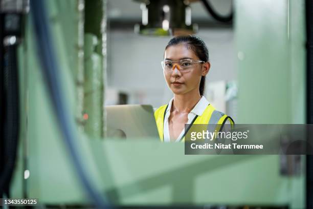 easy online production planning scheduling. female production planning engineer holding a laptop in front of automated steel press machine. she has skilled in planning, material forecasting, and machine utilization. - goud metaal stock pictures, royalty-free photos & images