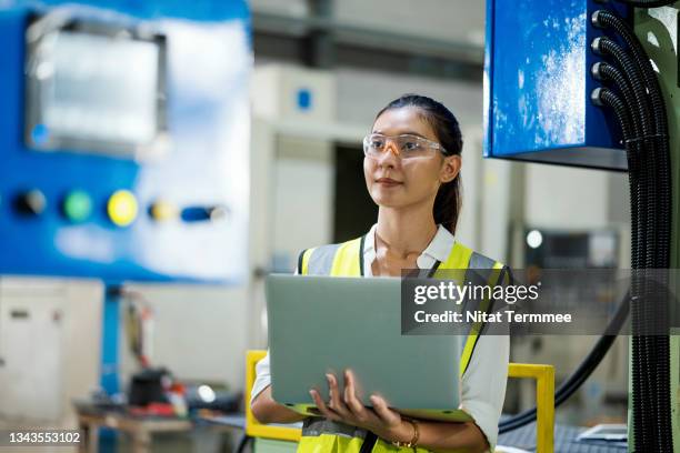 measure the productivity, effectiveness, or efficiency of machinery.  female engineer checking an automated mechanical press machine while standing and input data on a laptop in a production line of the manufacturing industry. - data processing stockfoto's en -beelden