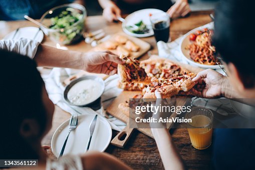 Nahaufnahme einer jungen Gruppe von Freunden, die vorbeikommen und Essen servieren, während sie zusammen genießen. Sie haben Spaß, plaudern und schlemmen Essen und Trinken auf der Dinnerparty Nahaufnahme einer jungen Gruppe von Freunden, die vorbeikommen und Essen servieren, während sie zusammen genießen. Sie haben Spaß, plaudern und schlemmen Essen und Trinken auf der Dinnerparty