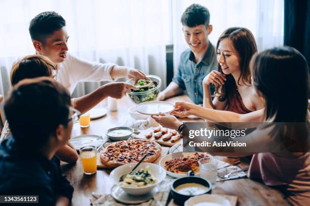 a young group of joyful friends having fun enjoying together, passing and sharing food across dining table at party - speed dating stock pictures, royalty-free photos & images