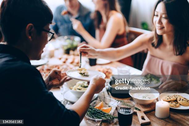 fröhliche junge asiatische frau, die dem mann pasta serviert. sie genießen zusammen, haben spaß, plaudern und schlemmen essen und trinken auf der party - eating yummy stock-fotos und bilder