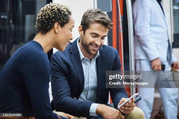 coworkers discussing over phone in subway train - man woman train station stockfoto's en -beelden