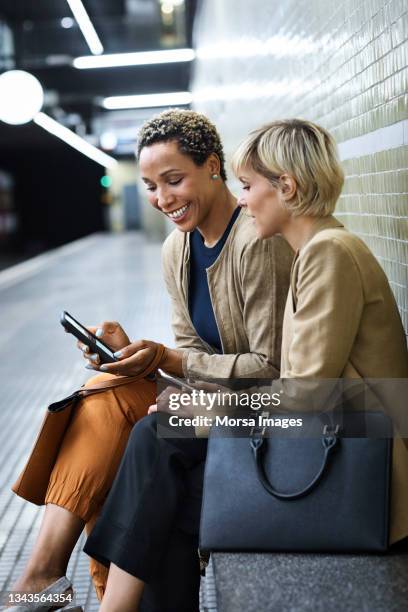 smiling colleagues using phone at subway station - gedeelde mobiliteit stockfoto's en -beelden