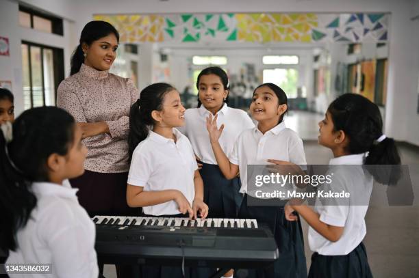 school children singing and playing keyboard musical instrument with their teacher in music room - enfant chant classe photos et images de collection