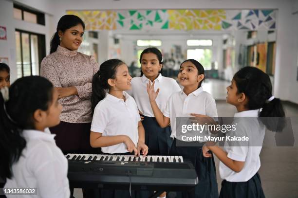 school children singing and playing keyboard musical instrument with their teacher in music room - indian kids singing stock pictures, royalty-free photos & images