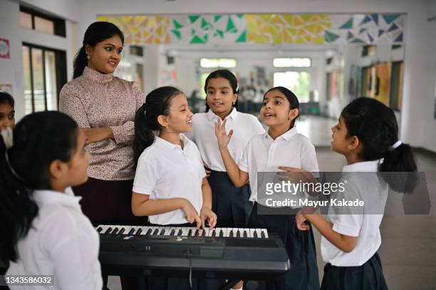 school children singing and playing keyboard musical instrument with their teacher in music room - indian music 個照片及圖片檔