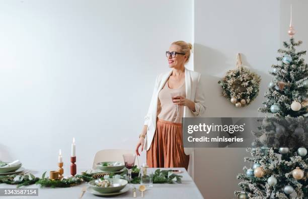 célébration de noël: femme joyeuse tenant un verre de vin à la maison - party host stock photos et images de collection