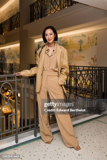 Chriselle Lim wears a gold chain CD necklace from Christian Dior, a beige shiny leather long oversized blazer jacket, a beige shirt, beige high waist...