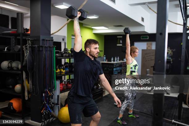 a fit young couple doing the dumbbell snatch at the gym - snatch weightlifting 個照片及圖片檔