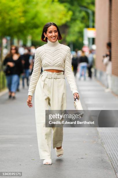 Alexandra Guerain wears a white latte braided wool turtleneck cropped pullover, beige belted ribbed large pants, a beige matte leather handbag from...