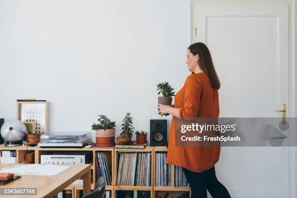 beautiful overweight woman standing in her home office, holding a flowerpot - carrying pot plant stock pictures, royalty-free photos & images