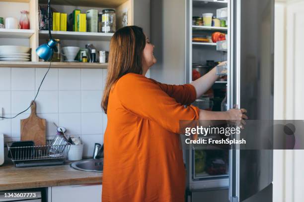 happy plus size woman preparing breakfast in the kitchen, taking something from the fridge - leftover stock pictures, royalty-free photos & images