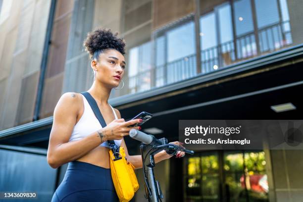 mixed race young girl standing on the street with electric scooter while using smart phone - step well stockfoto's en -beelden