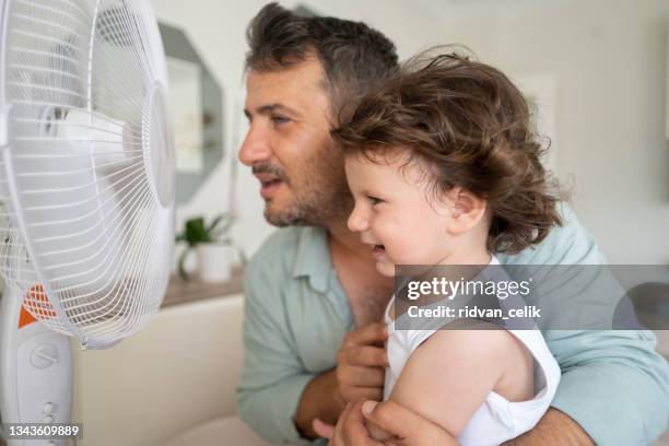 father child is front of electric fan on hot summer day - air conditioner family stock pictures, royalty-free photos & images