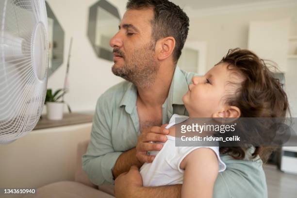 father child is front of electric fan on hot summer day - electric fan stock pictures, royalty-free photos & images