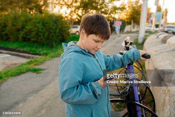 a teenager boy 12 years old pays for the rental of a scooter on the street using a mobile application - 10 11 years boy stockfoto's en -beelden