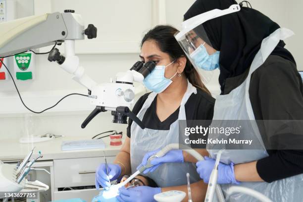 a female indian dentist, indian dental nurse  and indian patient in a modern dental surgery. the dentist is carrying out a procedure on the patient who is lying back in the dentists chair - in dentist chair stock pictures, royalty-free photos & images