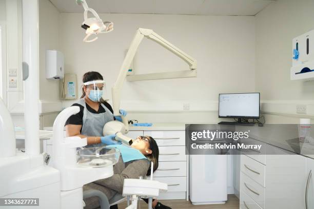 indian dentist and patient in a modern dental surgery. the dentist is carrying out a procedure on the patient who is lying back in the dentists chair. the dentist positions the x-ray camera - femalefocuscollection stock-fotos und bilder