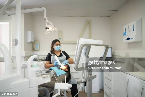 an indian dentist and indian patient in a modern dental surgery. the dentist is carrying out a dental imaging procedure on the patient who is lying back in the dentists chair whilst looking at a modern interactive touchscreen - femalefocuscollection stock-fotos und bilder